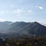 A small village nestled in a valley beneath rolling green mountains under a blue sky