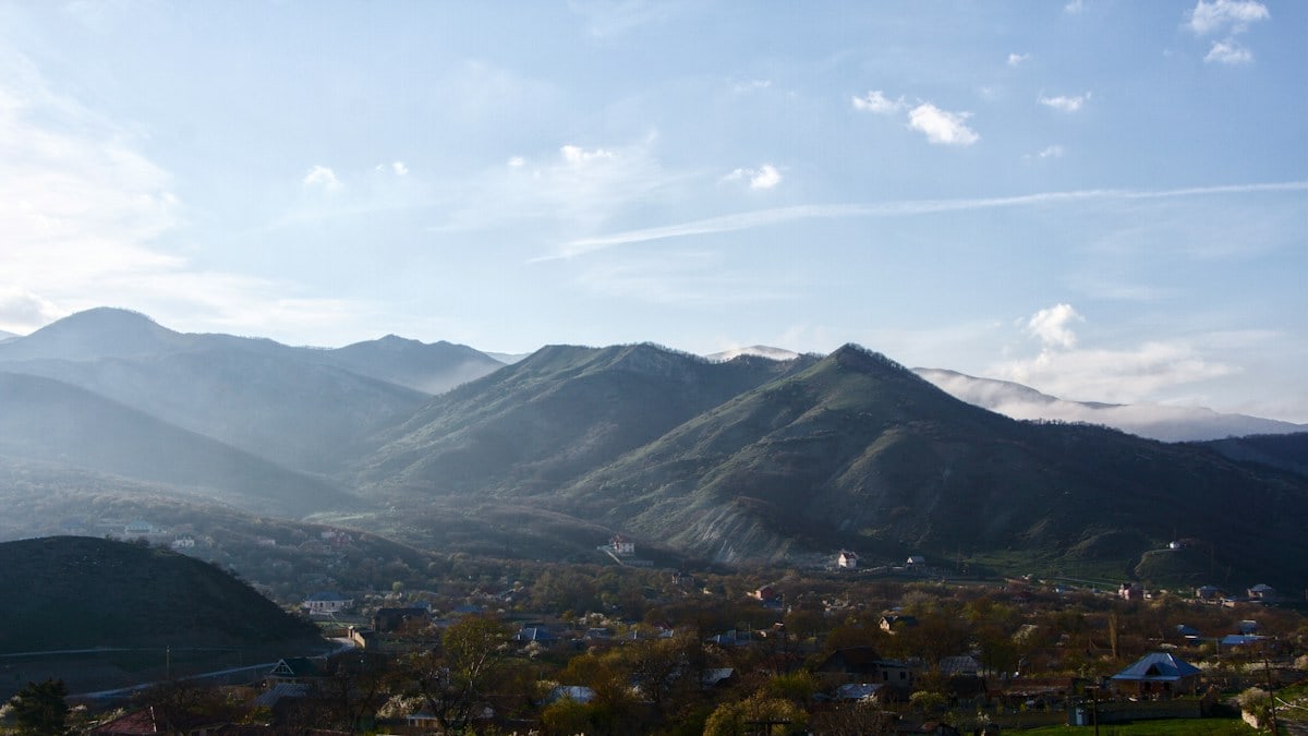 A small village nestled in a valley beneath rolling green mountains under a blue sky